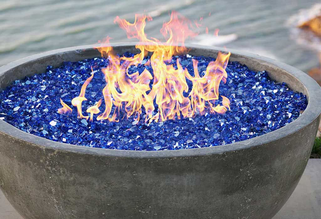 A close up shot of a lit concrete fire bowl with blue fire glass.