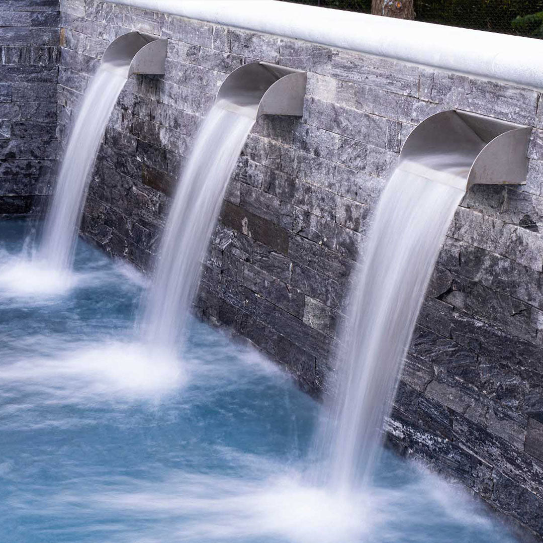 The Radius Pool Scupper installed on a pool wall with ledge stone.