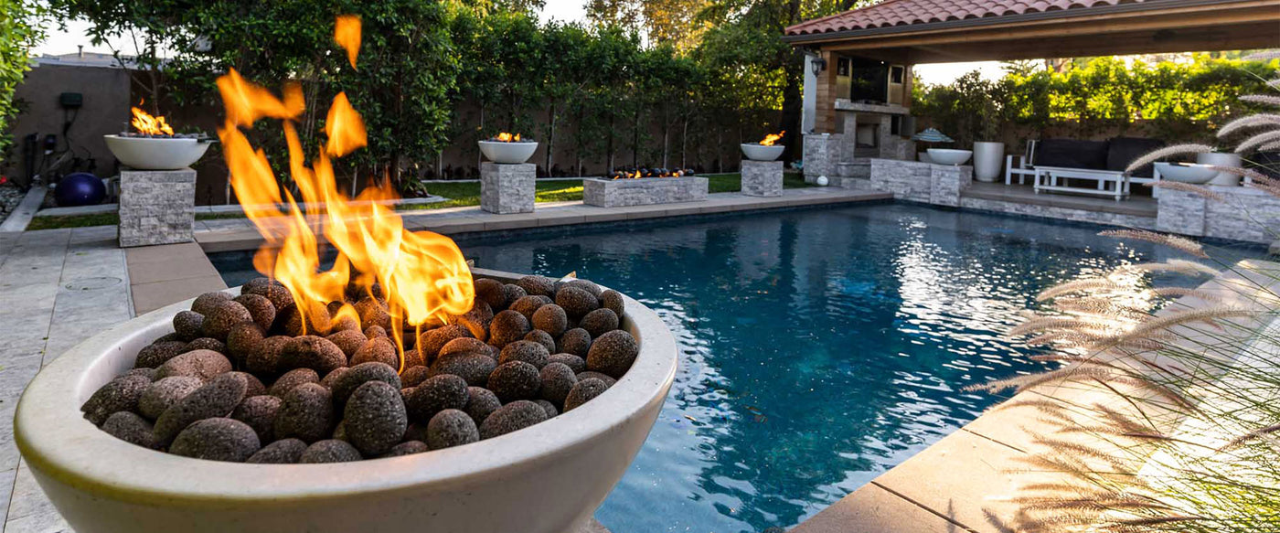 A close up shot of the Sedona Fire Bowl that's lit. It's on a pedestal around a pool. In the background you can see that there are 7 others around the pool and a large rectangular fire table.